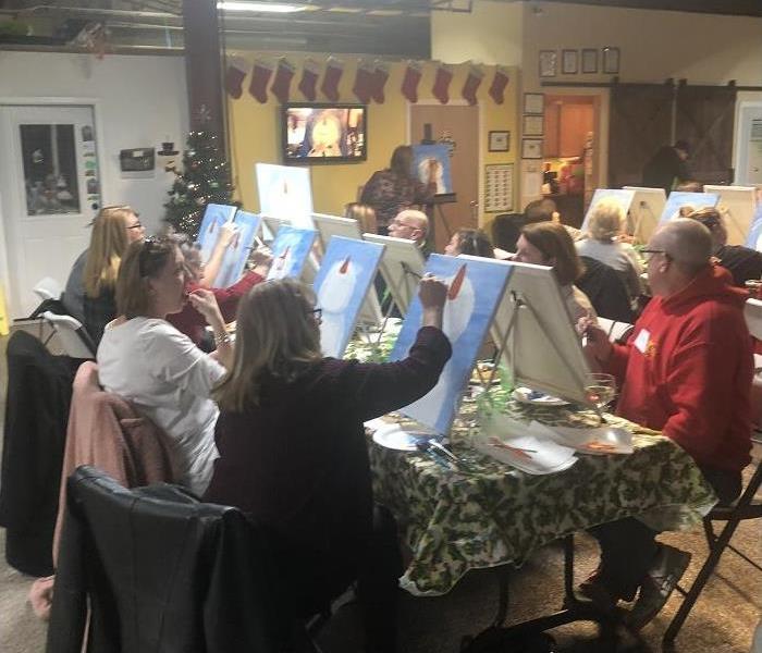 several people sitting around a table, each painting a canvass